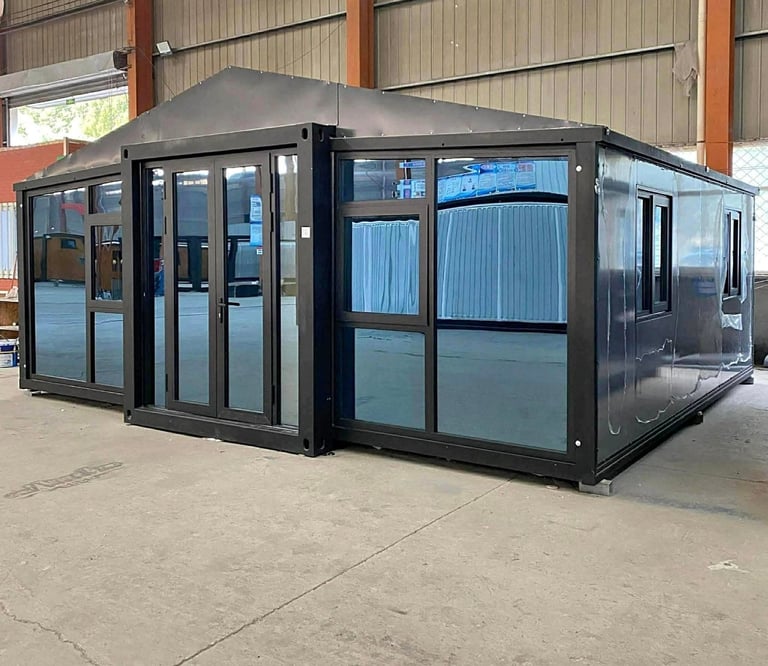 Black modular container building with glass windows and doors displayed in an industrial warehouse setting