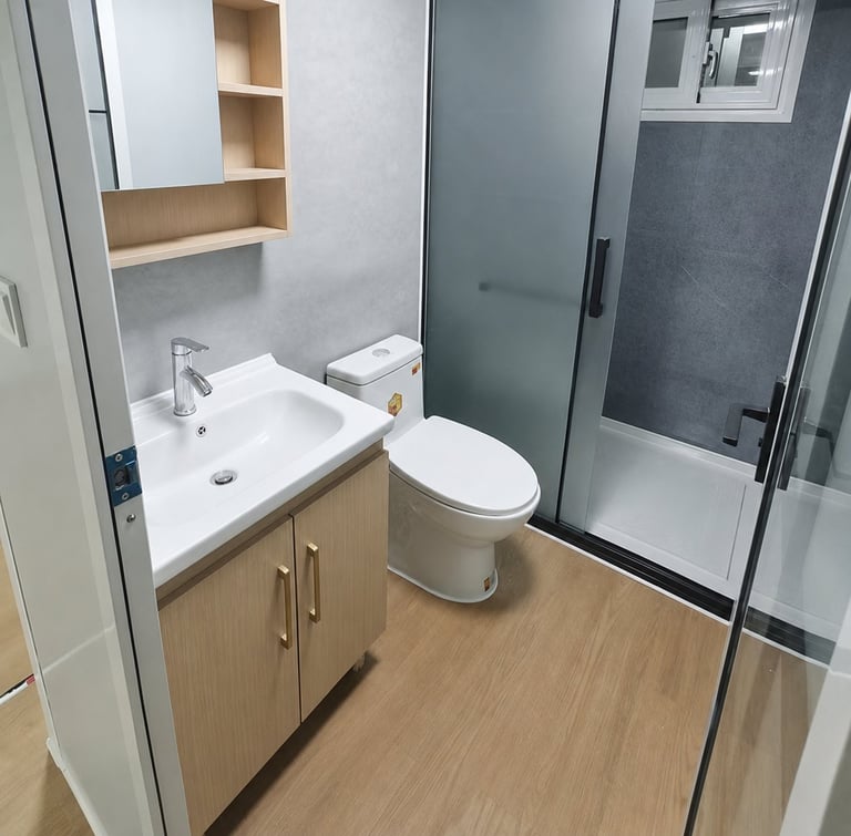 Modern bathroom with wooden vanity, white sink, toilet, and glass shower enclosure with gray tile walls