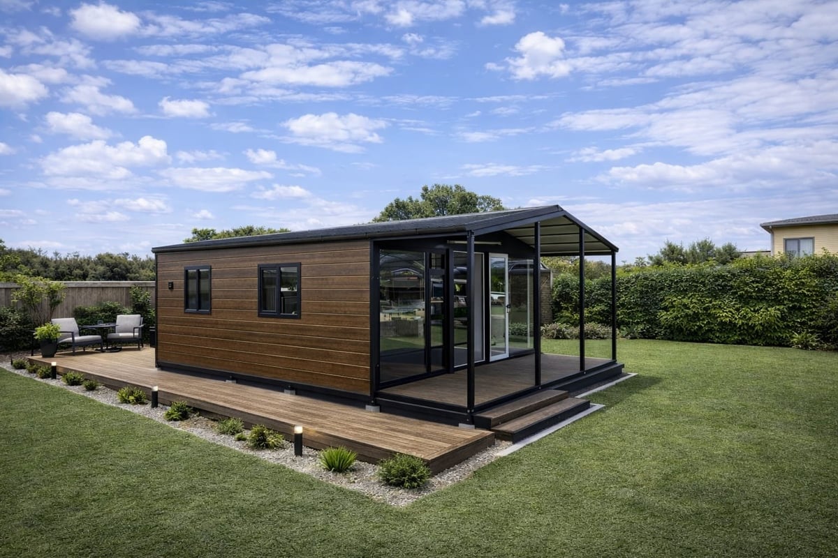 Modern tiny house with wood cladding and black frame on wooden deck in a grassy field under blue sky
